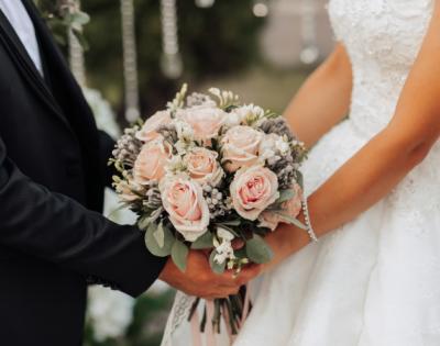 A groom (left) and a bride (right) both holding onto a pink bouquet of flowers